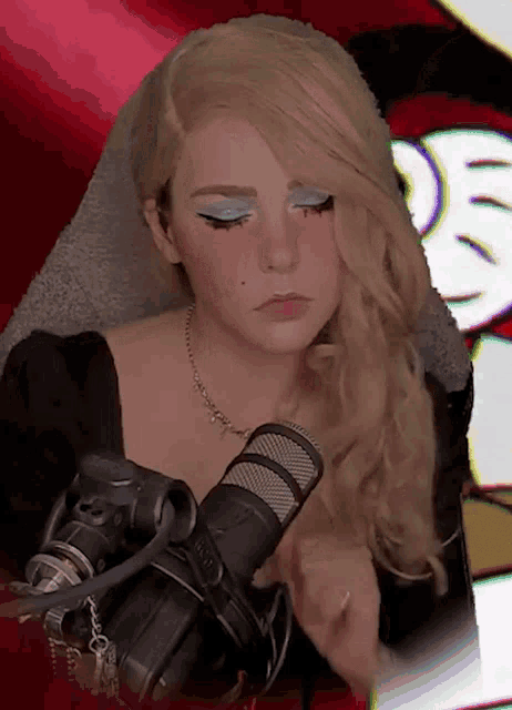 a woman with blonde hair is sitting in front of a microphone with a necklace around her neck and a ring on her finger