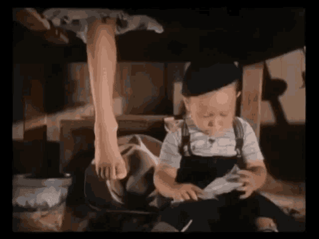 a little boy is sitting under a table with a woman 's foot hanging over his head .
