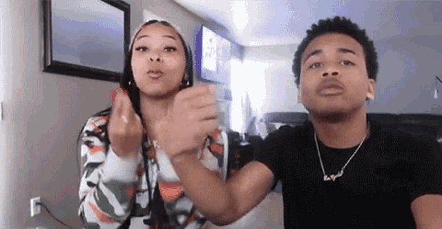 a man and a woman are standing next to each other in a living room giving the middle finger .