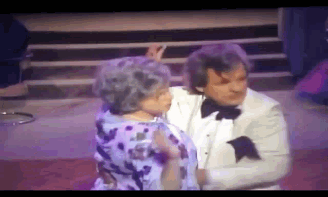 a man in a tuxedo is dancing with a woman in a purple dress