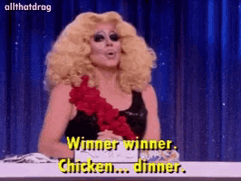 a drag queen is sitting at a table and says " winner winner chicken dinner "