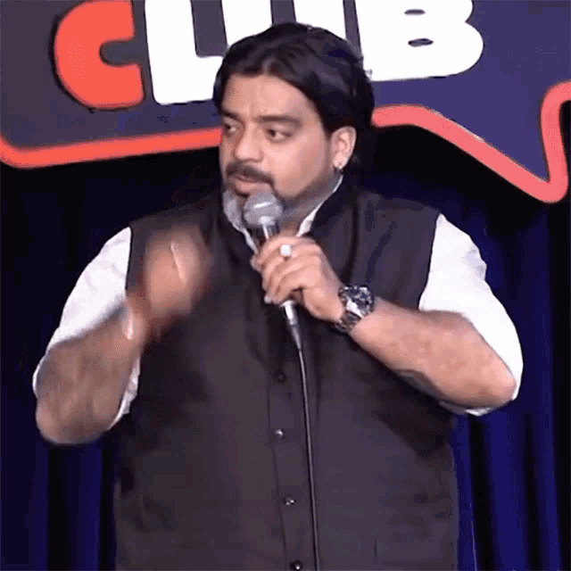 a man stands in front of a microphone in front of a club sign