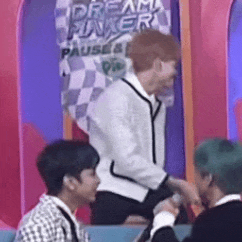 a group of young men are sitting on a stage in front of a sign that says dream maker .