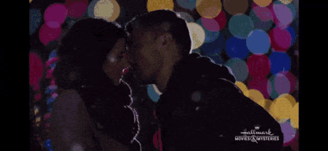 a man and a woman kissing in front of christmas lights from hallmark