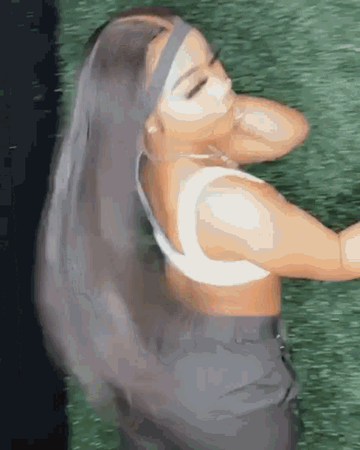 a woman wearing a headband and a crop top is laying on the grass .