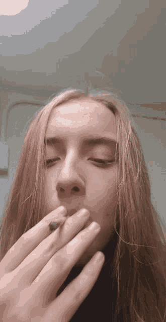 a girl with long hair is smoking a cigarette with her eyes closed