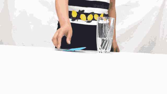 a person is holding a blue straw over a glass of water .