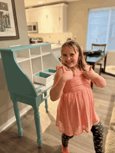 a little girl giving a thumbs up in front of a desk