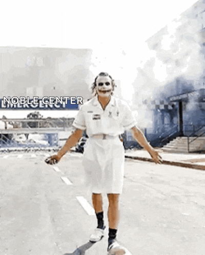 a man dressed as the joker is walking down the street with his arms outstretched .