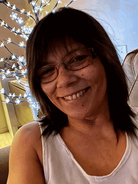 a woman wearing glasses and a white tank top smiles at the camera