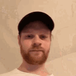 a man with a beard wearing a baseball cap and a white shirt .