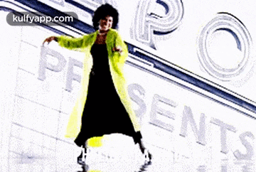 a woman in a yellow coat is dancing in front of a sign that says presents