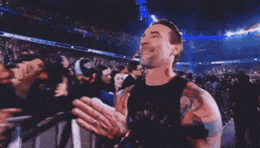 a man in a black tank top with a tattoo on his arm stands in front of a crowd of people