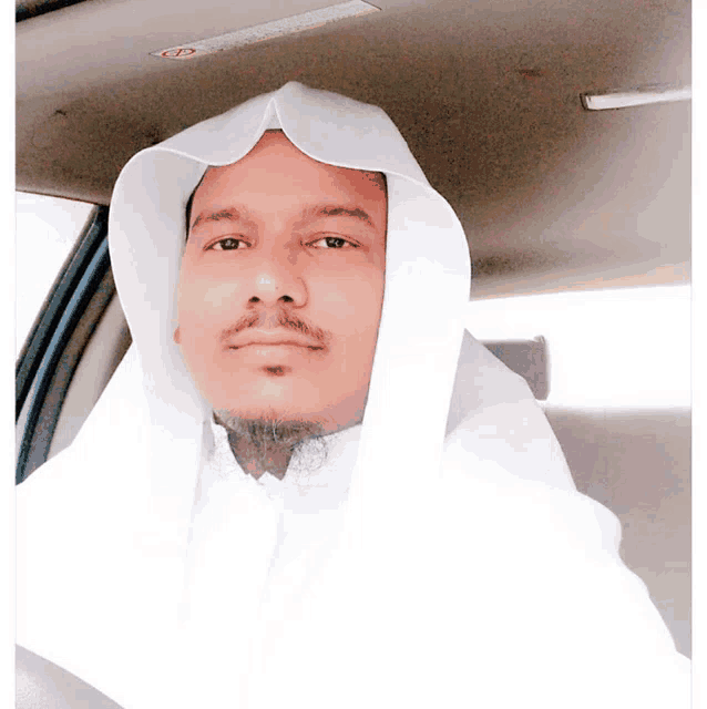 a man in a white robe is sitting in a car with a warning sign on the ceiling