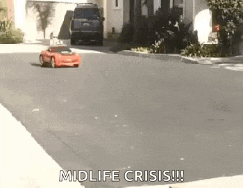 a red toy car is driving down a street with the words `` midlife crisis '' written on it .