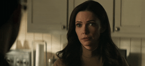 a woman in a brown turtleneck sweater looks at a man in a kitchen
