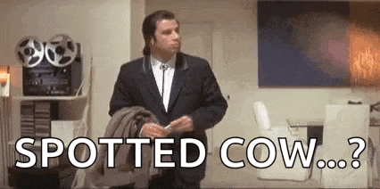 a man in a suit and tie is standing in a room with the words `` spotted cow ... ? '' .