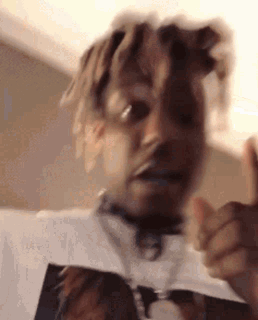 a man with dreadlocks is giving a thumbs up and wearing a white shirt with a picture of a horse on it .