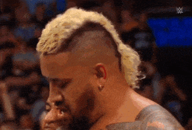 a man with a mohawk and a beard is standing next to another man in a wrestling match .