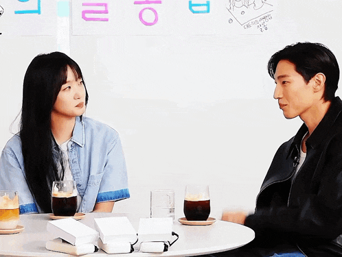 a man and a woman are sitting at a table with a sign on the wall that says ' i love you '