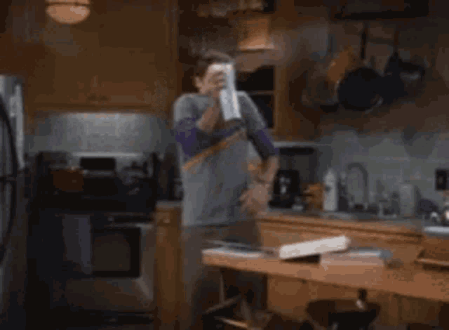 a man is standing in a kitchen holding a spray bottle over his face .