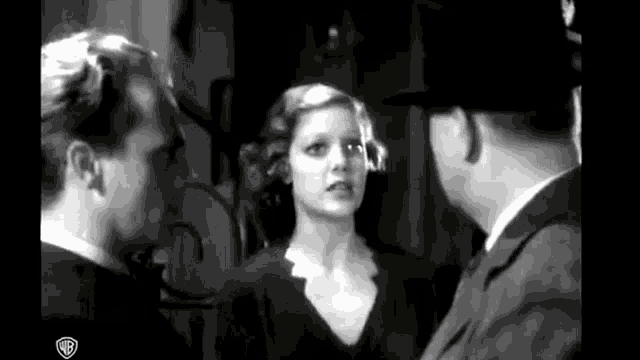 a black and white photo of a man and a woman talking to each other in a room .