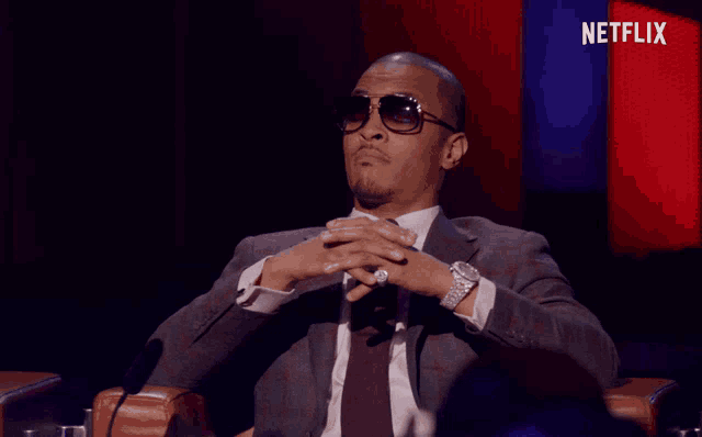 a man in a suit and sunglasses is sitting in front of a netflix sign