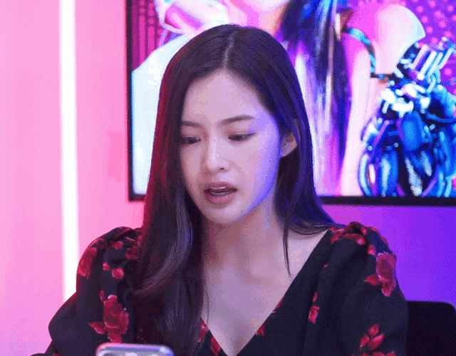 a woman in a black and red floral top looks at her phone