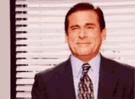 a man in a suit and tie is standing in front of a window with blinds .