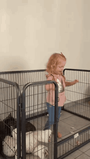 a little girl in a pink shirt is standing in a wire cage