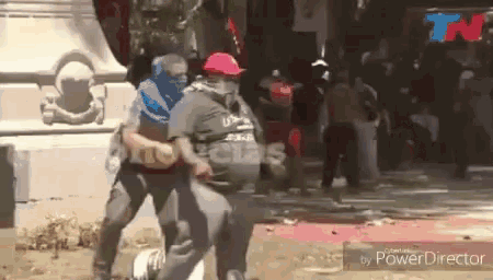 a man wearing a red hat and a mask is being held by another man in a crowd .