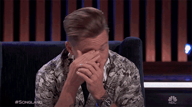 a man covering his face with his hands while watching a show called songland on nbc
