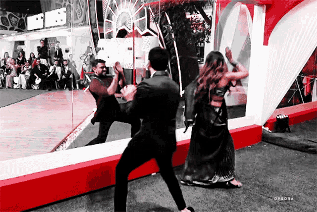 a man in a suit and a woman in a black dress are dancing in front of a mirror with the words epsora below them