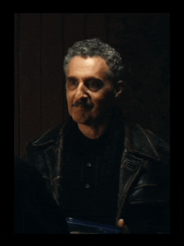 a man with a mustache is wearing a black shirt and a brown leather jacket