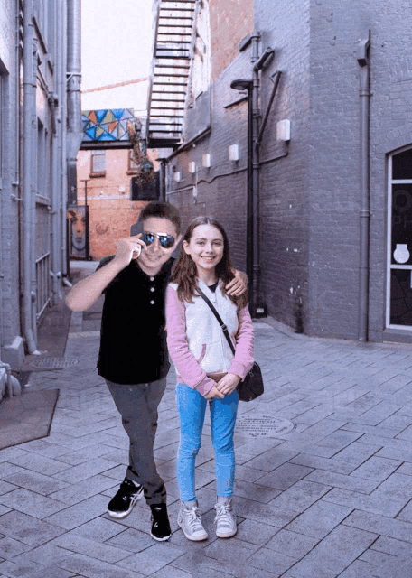 a boy and a girl are posing for a picture in a alleyway