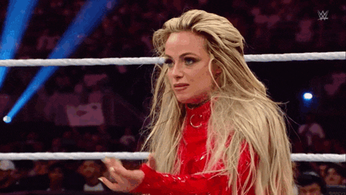 a woman in a red dress is standing in a wrestling ring with her hands outstretched .