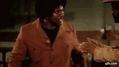 a man in a red jacket is talking to another man in a hat while another man shakes his hand .
