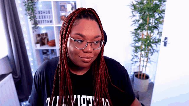 a woman wearing glasses and a t-shirt that says ' queens ' on it