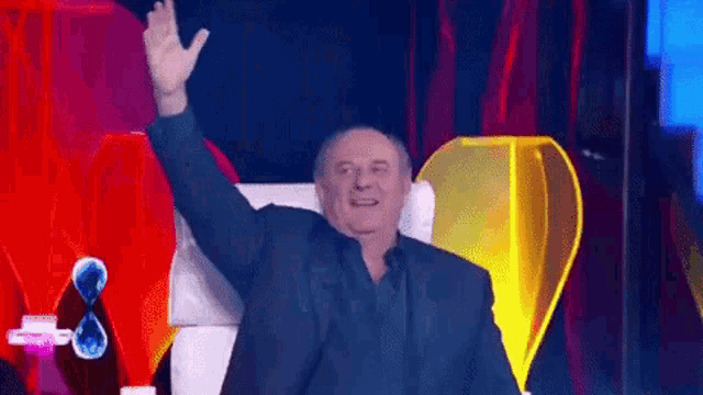 a man in a suit is sitting in a chair with his hand up in the air .