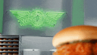 a chicken sandwich is being prepared in front of a neon sign for wing stop