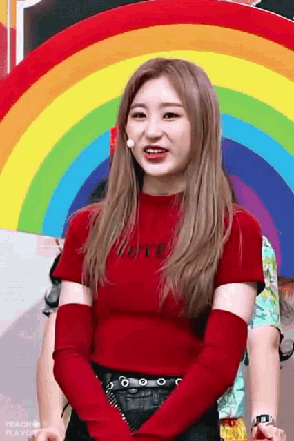 a girl in a red shirt with the word love on it stands in front of a rainbow