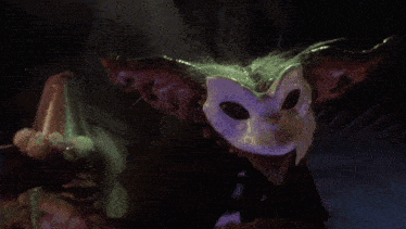 a gremlin is wearing a cat mask and holding a claw
