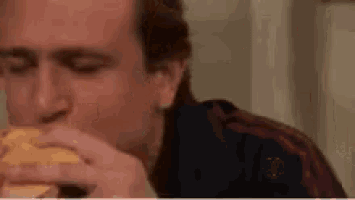 a man is eating a hamburger with his eyes closed in a kitchen .