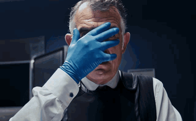 a man wearing blue gloves covers his face with his hand