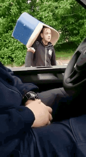a man is carrying a bucket on his head while sitting in a car