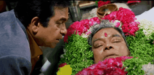 two men are looking at a man laying in a coffin with flowers around it