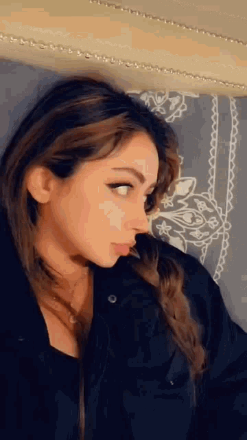 a woman in a black jacket is sitting on a bed and looking down .