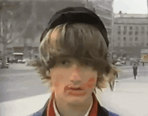 a young man wearing a hat and red paint on his face is standing on a street .