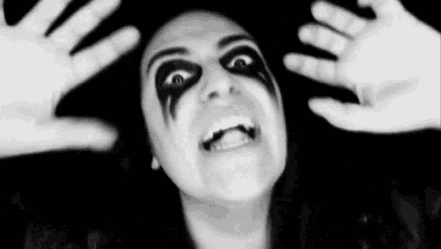 a woman with black paint on her face is making a funny face with her hands on her head .