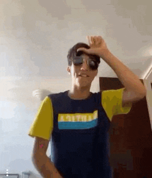 a young man wearing sunglasses and a t-shirt is dancing in a room .